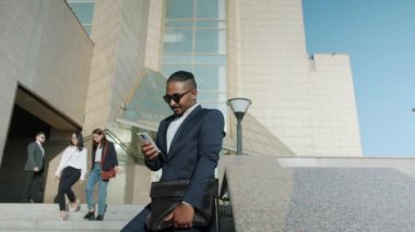 Takım elbiseli Orta Doğulu işadamı akıllı telefon kullanarak ofis merkezinin dışındaki ekrana dokunuyor.