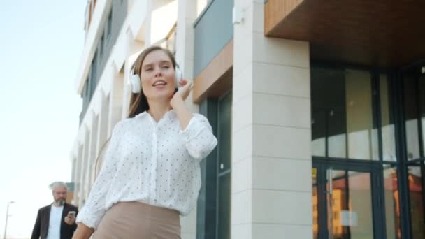Dolly záběr veselý businesswoman na sluchátka chůze venku tanec baví ve městě — Stock video