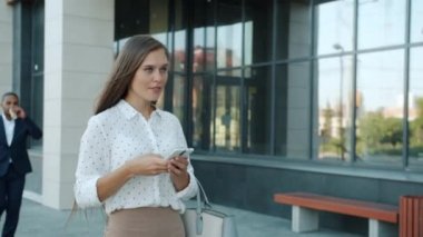 Modern ofis merkezinde akıllı telefon kullanarak yürüyen hırslı genç bir iş kadınının Dolly çekimi.