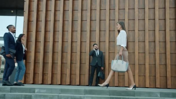 Vista lateral de hermosa joven mujer de negocios caminando al aire libre a lo largo del moderno centro de oficina — Vídeo de stock