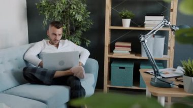 Cep telefonuyla konuşan ve bilgisayarını evde çalışan çekici bir adamın portresi.