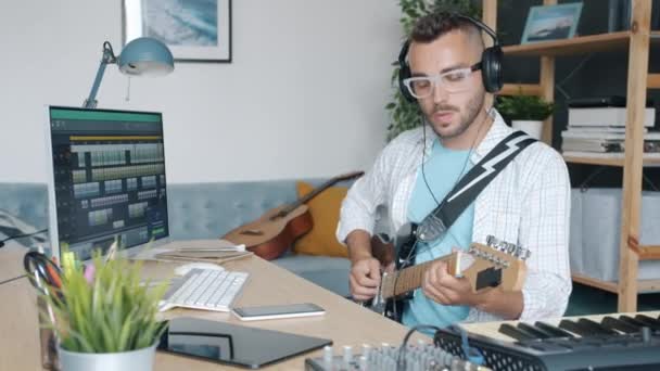 有创意的音乐家头戴耳机在室内弹奏电吉他，并在工作室里使用电脑 — 图库视频影像