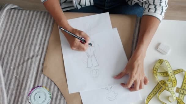 Kvinnlig hand ritar nya kläder på papper skapar fashionabla plagg vid bordet — Stockvideo