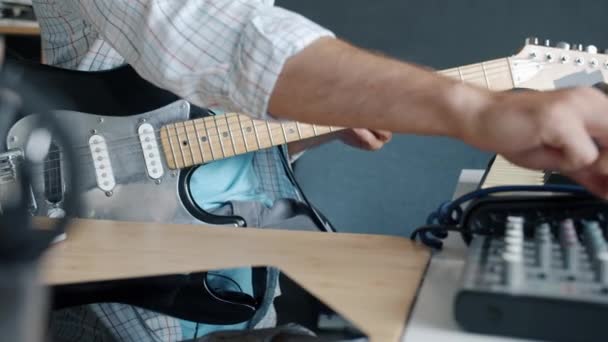 Primer plano de la mano usando el equipo de mezcla de sonido y luego tocando la guitarra eléctrica mientras el músico disfruta de la práctica en el estudio — Vídeo de stock