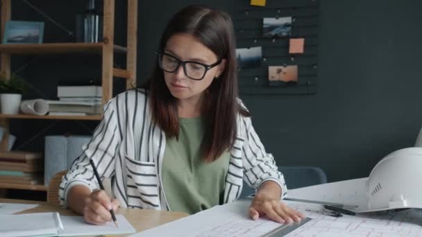 Serious female architect measuring construction plan with tools and writing working in office — Stock Video