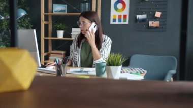 Moda tasarımcısı cep telefonuyla iş konuşuyor ve apartmandaki projede bilgisayar kullanıyor.