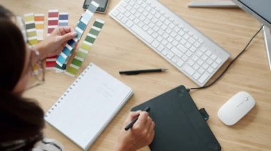 Dijital tabletle çalışan genç bir kadının ofisin içinde çizim yaparken yüksek açılı görüntüsü