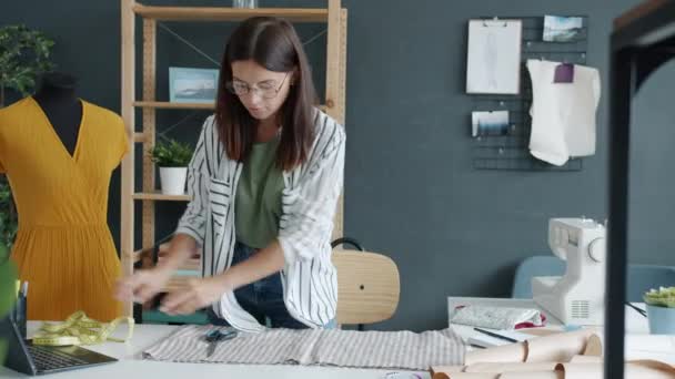 Jonge naaister maakt nieuwe kledingstuk meetstof met sjabloon geconcentreerd op handwerk in studio — Stockvideo