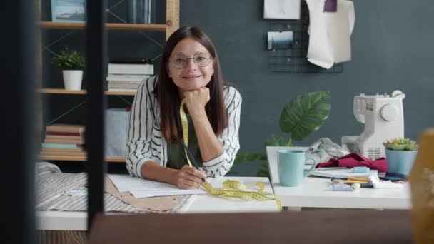 Retrato en cámara lenta de la atractiva joven diseñadora de ropa sonriendo mirando a la cámara en el estudio — Vídeos de Stock