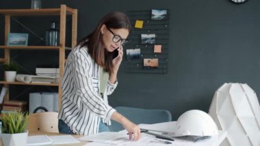 Güzel bayan mimar inşaat projesini cep telefonuyla tartışıyor bina planlarına bakıyor.