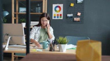 Genç bayan tasarımcı cep telefonuyla konuşuyor ve bilgisayar kullanarak renk paletlerine bakıyor