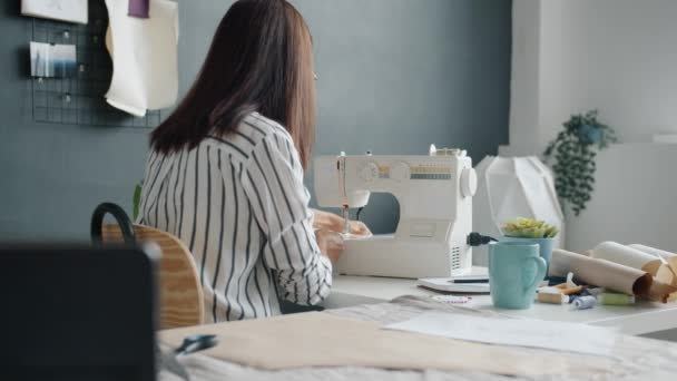 Веселая молодая женщина создает новую одежду с швейной машинкой, работающей только в ателье — стоковое видео