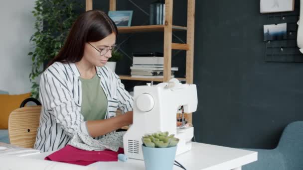 Trage beweging van pensive naaister maken van nieuw kledingstuk met naaimachine thuis — Stockvideo