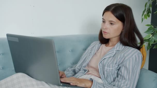 Femme pensive travaillant à la maison à l'aide d'un ordinateur portable tapant en regardant des documents assis sur un canapé confortable — Video