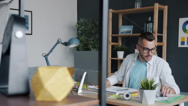 Retrato en cámara lenta de la escritura del diseñador de aplicaciones de teléfonos inteligentes utilizando el dispositivo y escribiendo con el ordenador en la oficina — Vídeo de stock