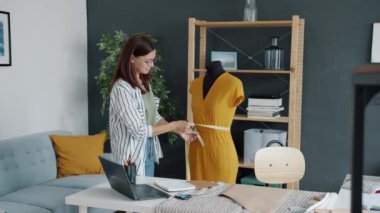 Evde tek başına çalışan mankenin üzerindeki genç terzi elbisesini yavaş çekimde ölçüyor.