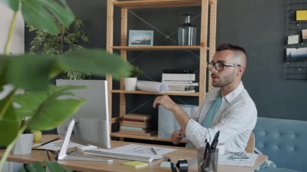 Портрет серьезного архитектора-мужчины, изучающего чертеж на бумаге и смотрящего на экран компьютера, работающего в квартире — стоковое видео