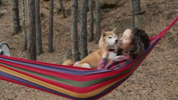 Portret van een mooie jonge vrouw ontspannen in hangmat in de herfst bos zoenen shiba inu hond — Stockvideo