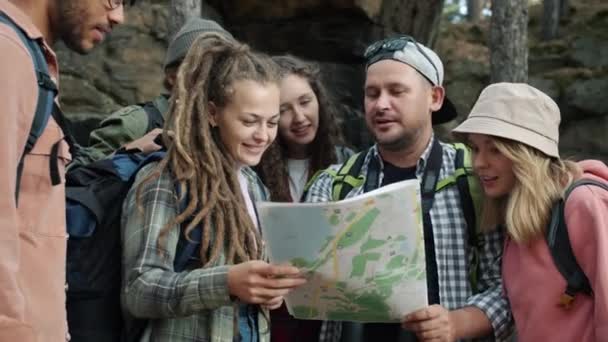 Amigos alegres turistas estudando mapa, em seguida, andando na floresta de outono verde — Vídeo de Stock