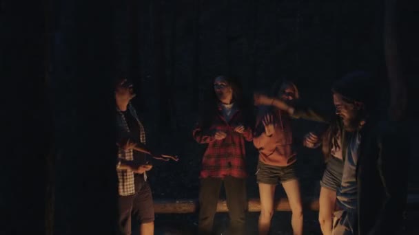 Happy young people dancing around fire in dark forest having fun and laughing enjoying music and beautiful nature. — Stock Video