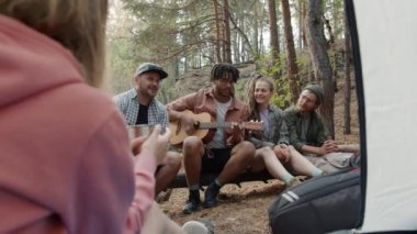 Neşeli turistler gitar çalıp gülüyor ve kamp alanında eğleniyorlar.
