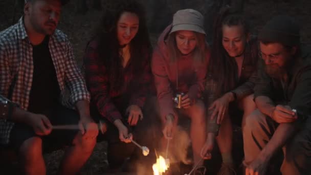 Πεινασμένοι ταξιδιώτες μαγειρεύουν ζαχαρωτά στη φωτιά τρώγοντας απολαμβάνοντας τη συζήτηση γύρω από τη φωτιά το βράδυ — Αρχείο Βίντεο