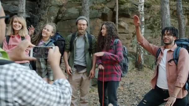 Παιχνιδιάρηδες τουρίστες διασκεδάζουν ποζάροντας γελώντας, ενώ ο τύπος τραβάει φωτογραφίες με κάμερα smartphone στο δάσος — Αρχείο Βίντεο