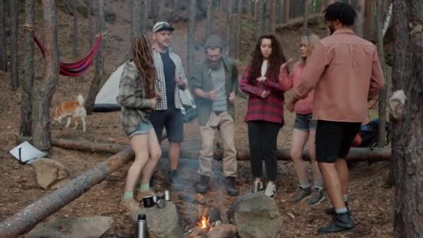 Retrato em câmera lenta de turistas alegres dançando ao redor da fogueira rindo se divertindo na floresta — Vídeo de Stock