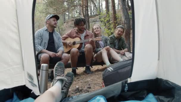 Mutlu genç kızlar ve erkekler kampta eğleniyor gitar çalıp gülüyorlar çadırda dinleniyorlar. — Stok video