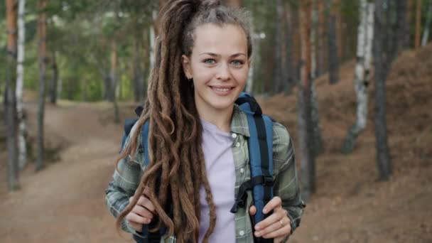 Медленный портрет милой молодой женщины с дредами, стоящими в лесу с рюкзаком — стоковое видео