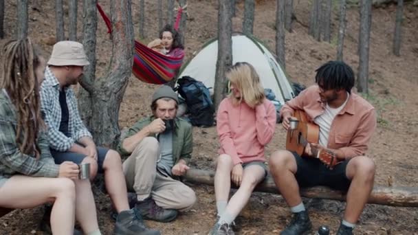 Ομάδα φίλων τουρίστες που μιλούν παίζοντας κιθάρα και αιώρηση στην αιώρα χαλάρωση στην κατασκήνωση στο δάσος φθινόπωρο — Αρχείο Βίντεο