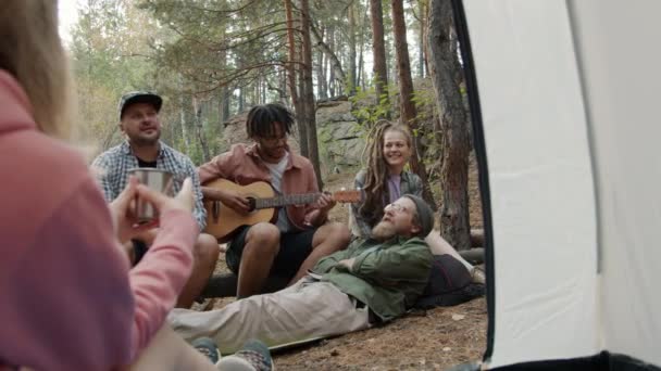 Çadırdaki kız, sonbahar ormanlarında gitar çalan ve çay içen bir grup arkadaşı dinliyor. — Stok video
