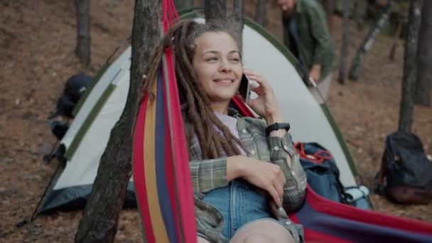 Heyecanlı genç bir kadın cep telefonuyla konuşuyor ve gülüyor hamakta dinleniyor ormanda. — Stok video