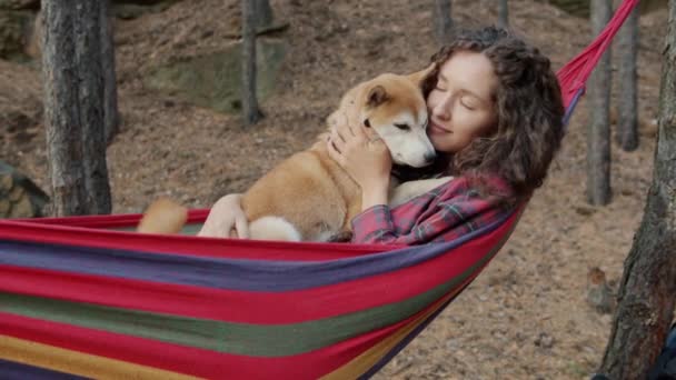 Gyönyörű fiatal hölgy ölelés aranyos shiba inu kutyus lengő függőágyban pihentető erdőben ősszel nap — Stock videók