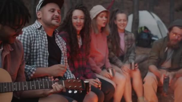 Afro-Amerikaanse man gitaar spelen terwijl vrienden toeristen zingen en dansen zitten rond vuur in het bos 's nachts — Stockvideo