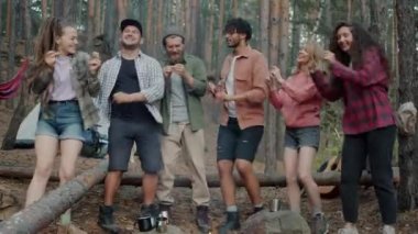 Neşeli kızların ve kamp alanındaki ormanda dans eden erkeklerin portresi doğa ve açık hava partilerinin tadını çıkarıyor.
