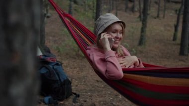 Neşeli kız turist duygularını paylaşıyor cep telefonuyla konuşuyor hamakta dinleniyor ormanda.