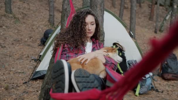Feliz turista femenina relajándose en hamaca acariciando adorable shiba inu perro disfrutando de la paz en el bosque de otoño — Vídeos de Stock