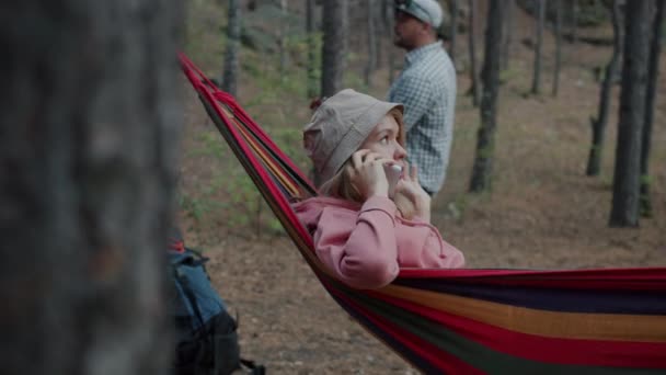 Cep telefonuyla konuşan çekici genç bir kadın sonbahar ormanlarında hamakta eğleniyor. — Stok video