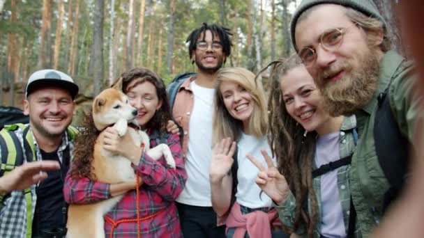 POV retrato de niñas y chicos excursionistas con perro tomando selfie en el bosque agitando las manos sonriendo — Vídeo de stock