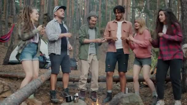 Lekfulla ungdomar dansar runt lägerelden i skogen under friluftsresan utomhus — Stockvideo