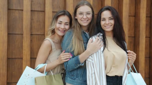 Retrato en cámara lenta de felices amigas sonriendo al aire libre sobre fondo de madera sosteniendo bolsas de compras — Vídeo de stock