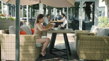 Çekici kız açık kafede kitap okuyor. Masada tek başına oturuyor.