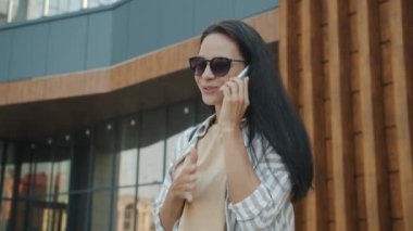 Neşeli esmerin portresi cep telefonuyla konuşuyor ve gülümsüyor modern şehrin dışında duruyor.