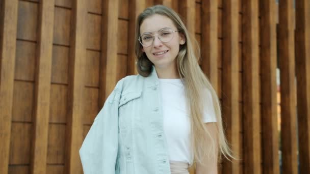 Ritratto al rallentatore di giovane donna felice con i capelli biondi che guarda la macchina fotografica e sorride in piedi all'aperto — Video Stock