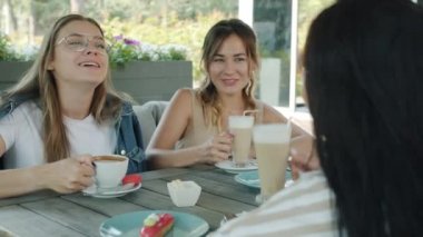 Bayan arkadaşlar çekici genç kadınlar bardaklarını tokuşturup kutlama konuşuyorlar yaz günü sokak kafesinde.