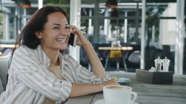 Young woman talking on mobile phone enjoying conversation smiling sitting in open air cafe outdoors — Stock Video