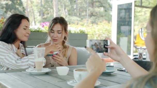 Друзья-игривые девушки позируют для камеры смартфона, веселятся в уличном кафе летом — стоковое видео