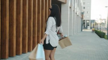 Alışveriş poşetleriyle gezen ve gülümseyen sevimli genç bir bayan.