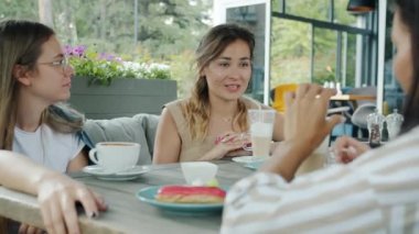 Mutlu bayan arkadaşlar sohbet ediyor. Dedikodu yapıyorlar. Yaz günü şehir parkındaki açık hava kafeteryasında oturuyorlar.